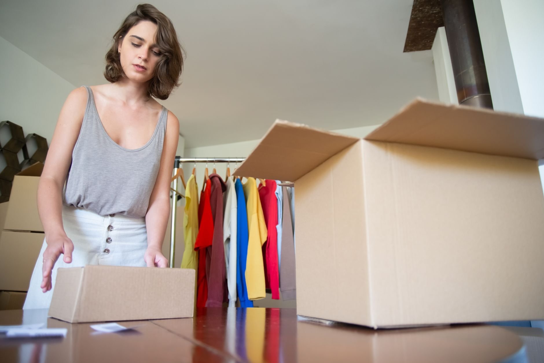 Woman packing boxes in a clothing store setting, organized for business and shipping.